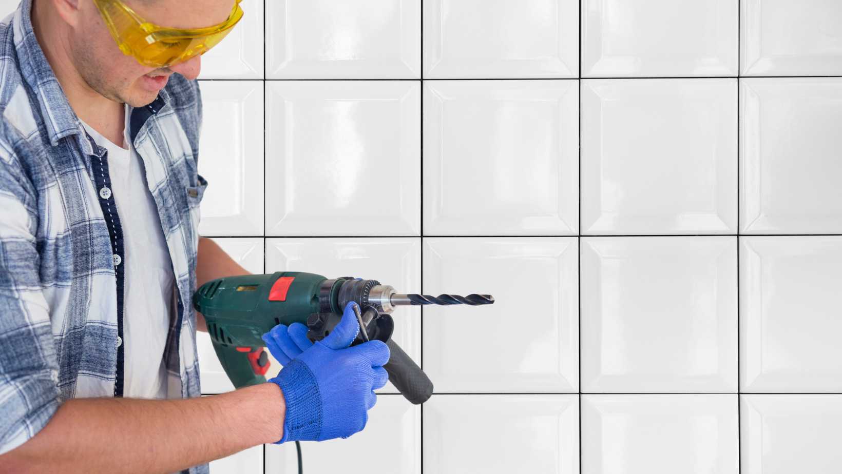 Homem com furadeira na mão em frente a uma parede de azulejos ilustrando o artigo sobre como furar azulejo com furadeira.